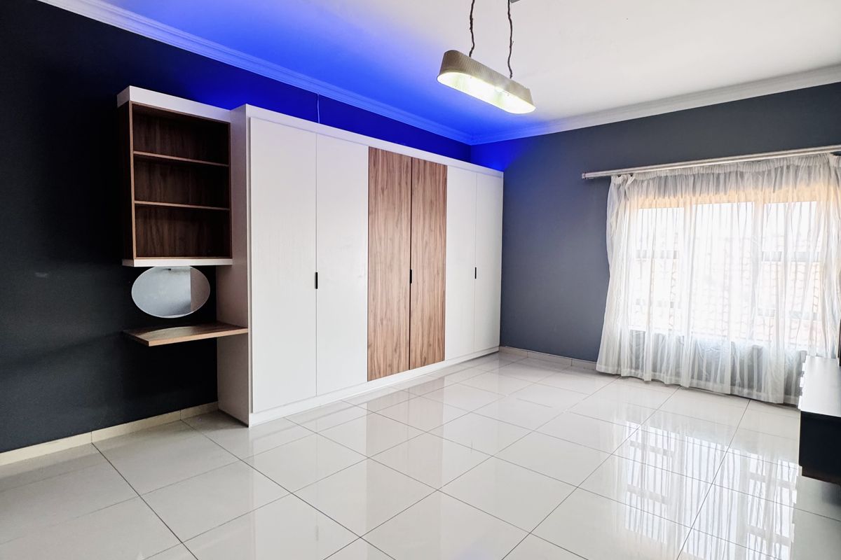 A spacious bedroom featuring large built-in wardrobes with integrated shelving and vanity, polished tile flooring, and modern recessed LED accent lighting.
