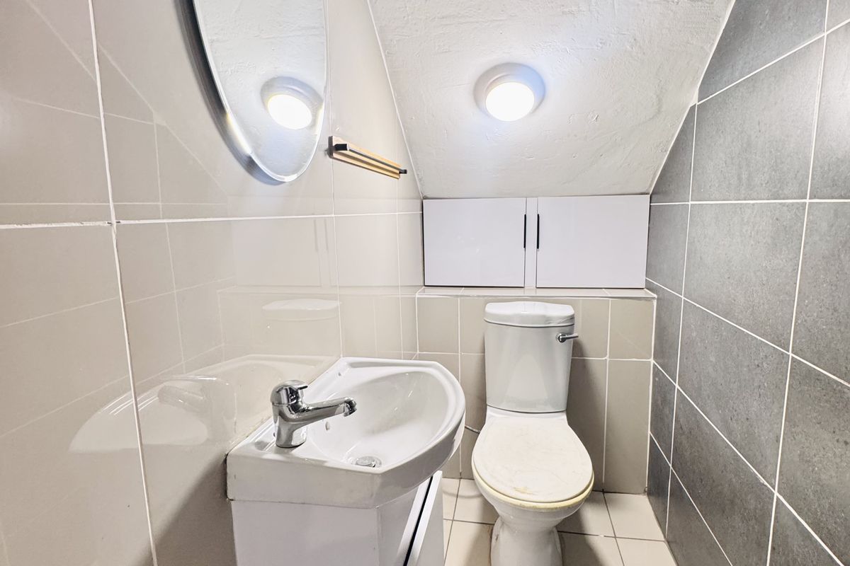 Compact bathroom featuring a modern vanity basin, toilet, and neutral wall tiling with contrasting grey feature tiles under a sloped ceiling.