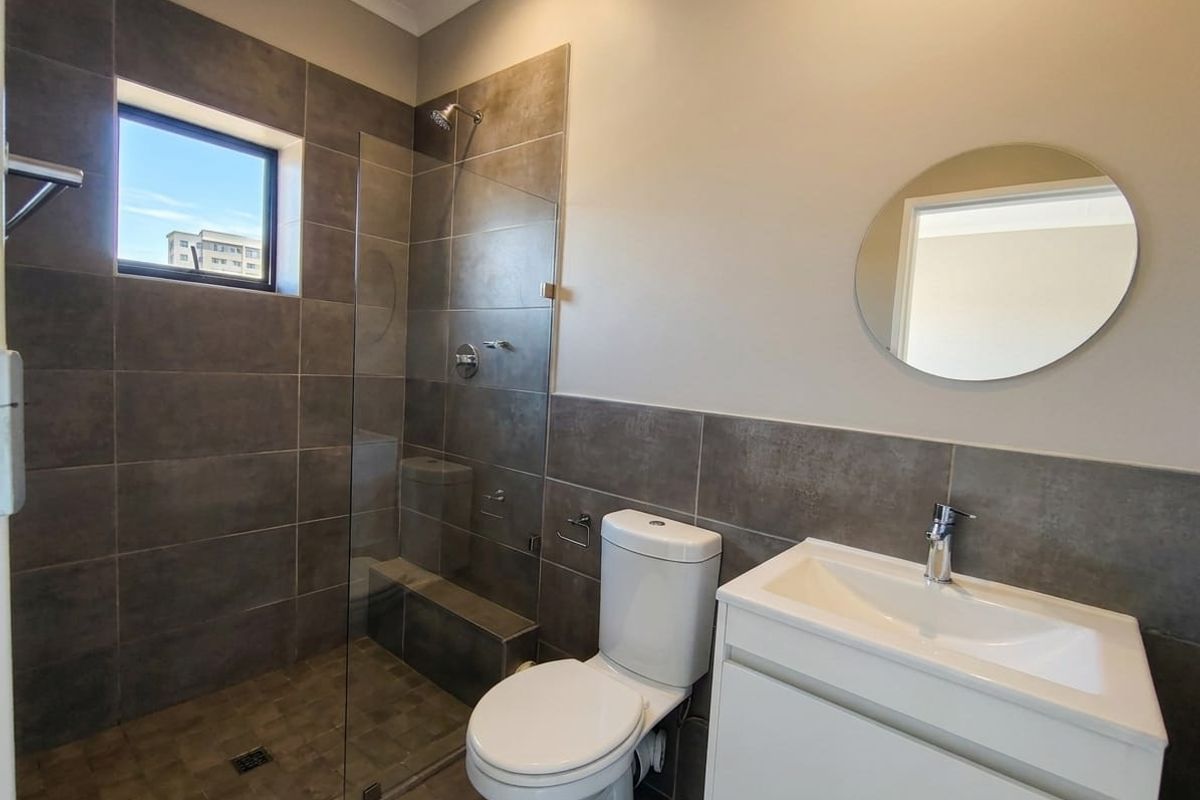 Modern bathroom featuring a walk-in shower with glass screen, dark grey wall tiles, a white vanity with basin, and a toilet.