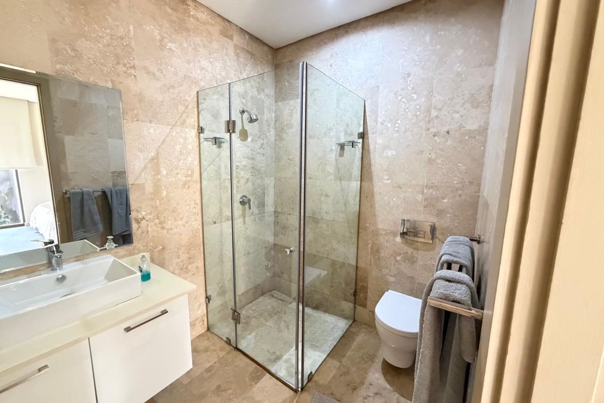 Modern bathroom featuring floor-to-ceiling travertine tiling, a frameless glass shower enclosure, a wall-mounted toilet, and a sleek vanity with a vessel sink.