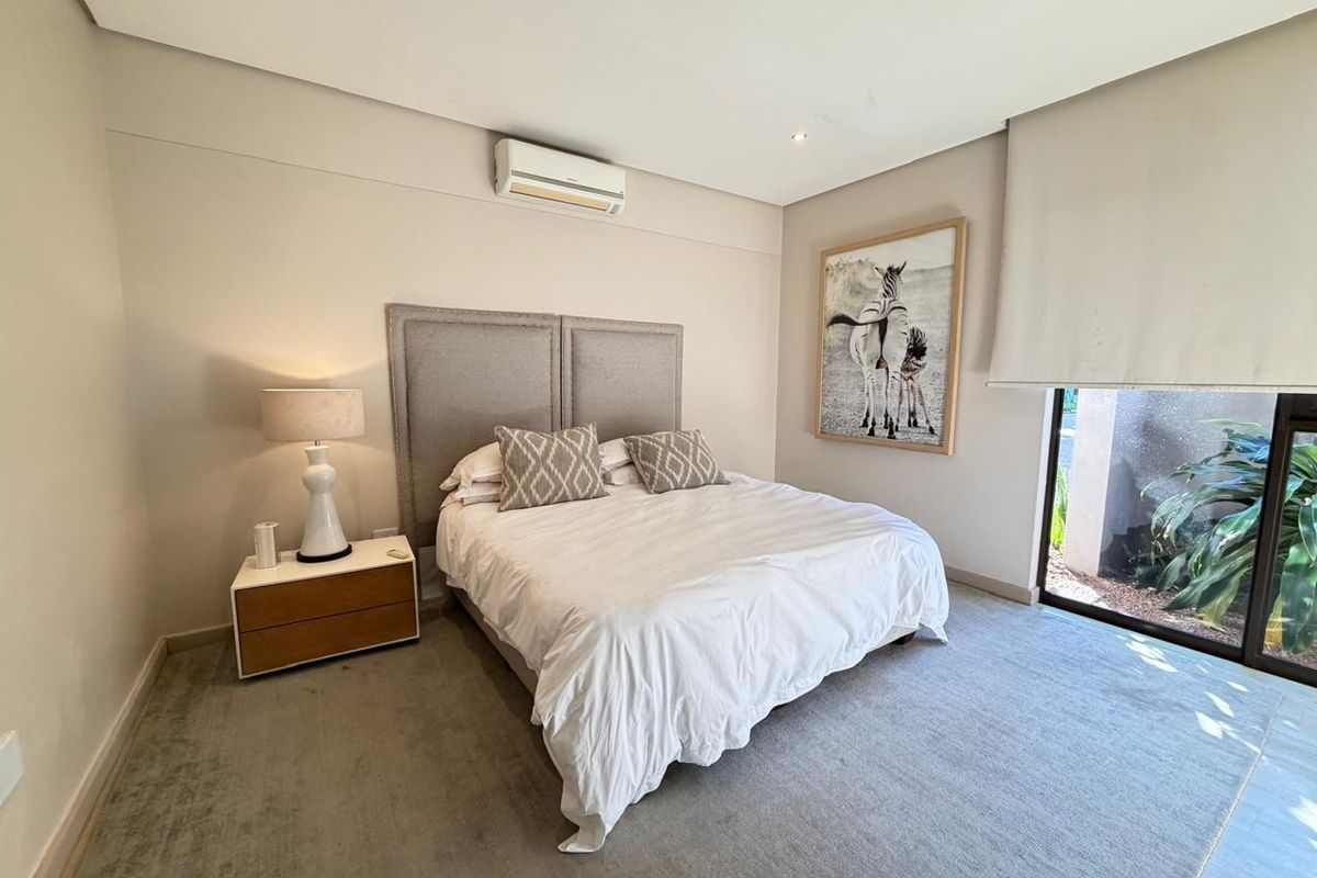 A well-maintained bedroom featuring neutral wall tones, recessed ceiling lighting, a wall-mounted air conditioning unit, and large sliding glass doors leading outdoors.