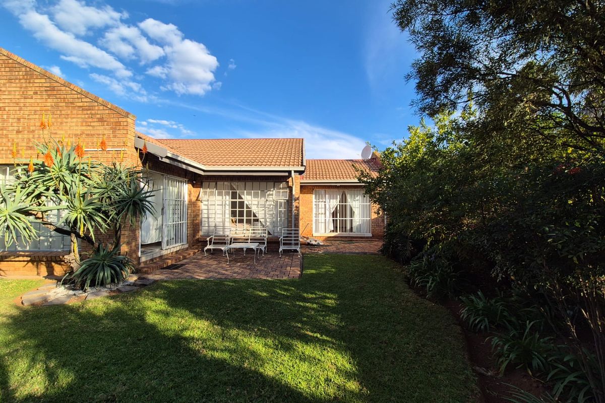 A well-maintained rear exterior view of the townhouse featuring a brick facade, tiled roof, paved patio area, and a landscaped garden.