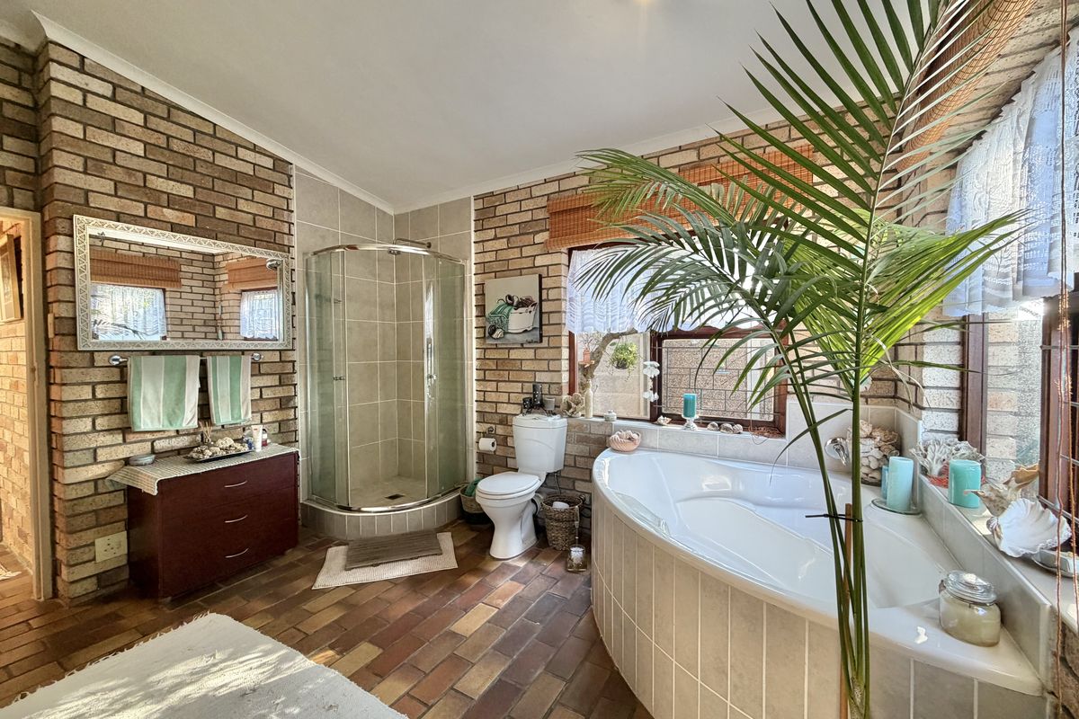 Spacious bathroom featuring a corner bathtub, separate glass-enclosed shower, and exposed brick walls with tiled flooring.