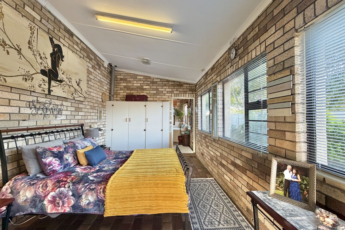 A bedroom featuring exposed brick walls, tiled flooring, built-in wardrobe storage, and large windows with fitted blinds.