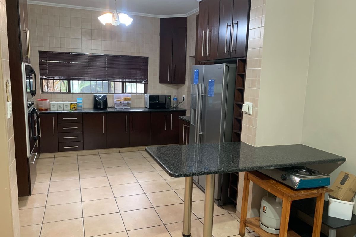 A functional kitchen featuring dark wood cabinetry, granite countertops, a breakfast nook, and tiled flooring with integrated appliance space.