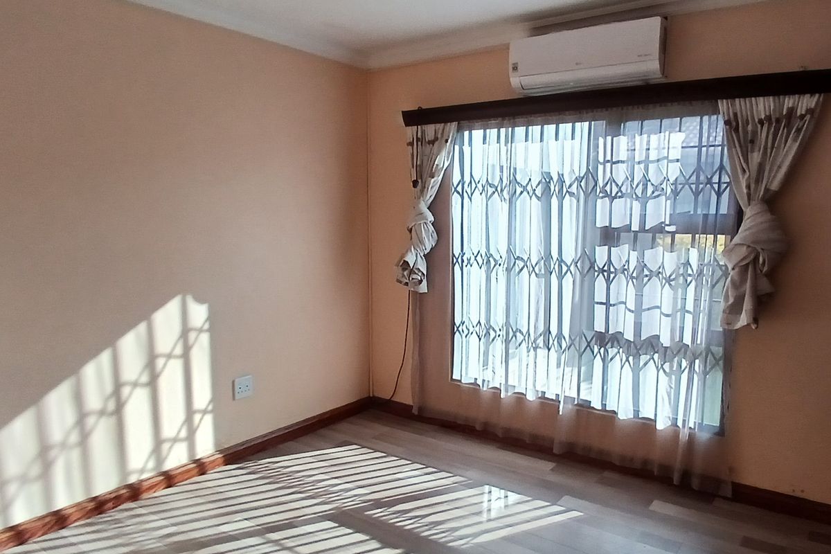 A bright bedroom featuring laminate flooring, a wall-mounted air conditioning unit, and a security gate installed over the window.