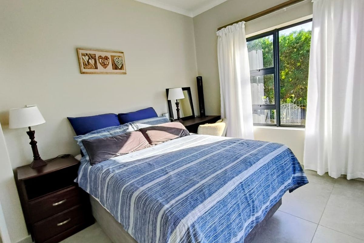 A bright and well-maintained bedroom featuring neutral wall tones, tiled flooring, and a large window allowing for ample natural light.