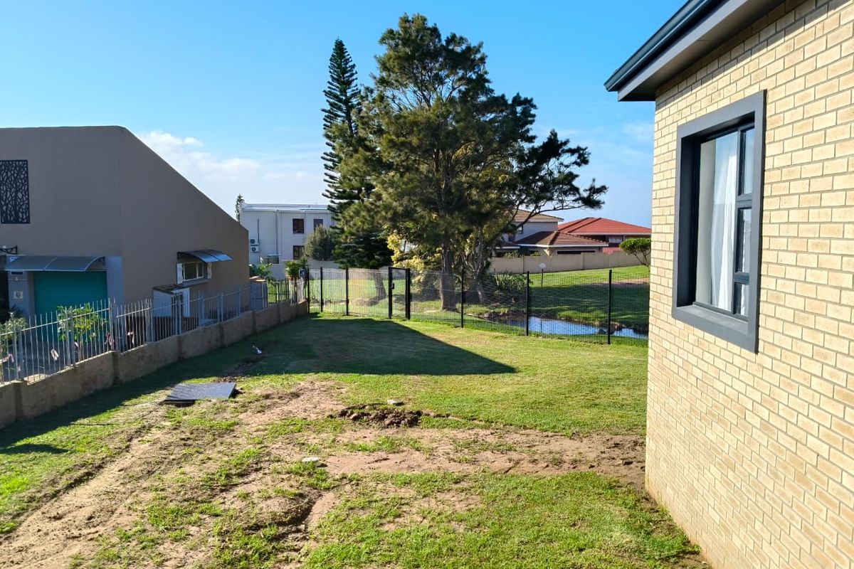 A view of the rear garden area featuring a brick exterior wall, perimeter fencing, and an open lawn space.