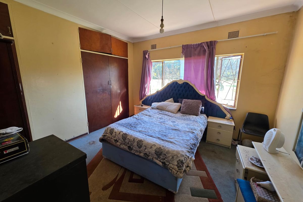 A bedroom featuring built-in wooden cupboards, large windows with security bars, and standard ceiling finishes.