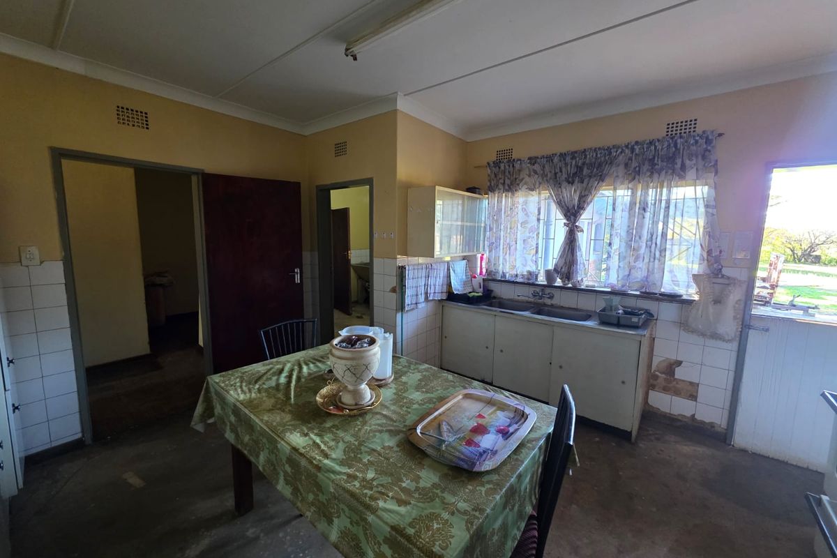A dated kitchen area featuring basic cabinetry, a stainless steel sink, and tiled splashbacks, requiring significant renovation and modernization.
