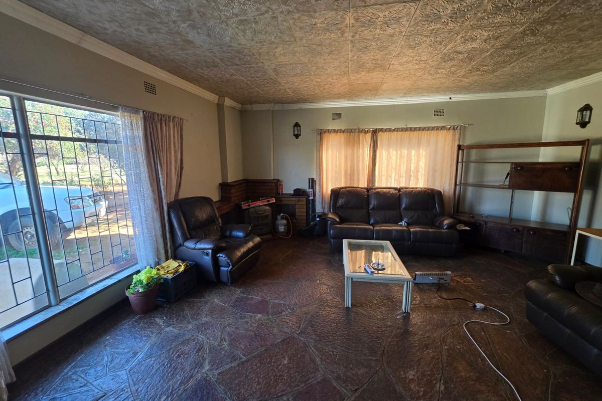 Spacious living room featuring unique stone flooring, decorative textured ceiling tiles, and large windows with security bars, offering a dated but functional layout.