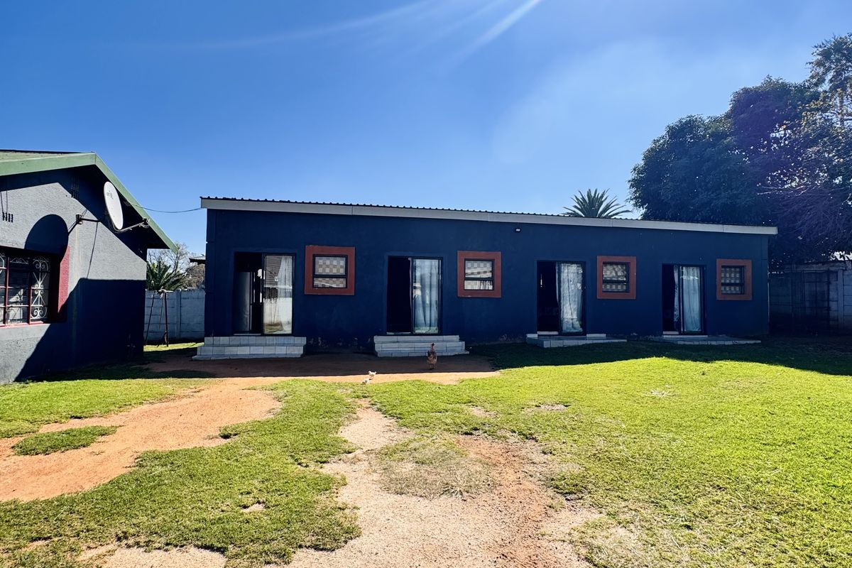 A view of the rear exterior of the property featuring a long building with multiple access points and a large grassed yard.