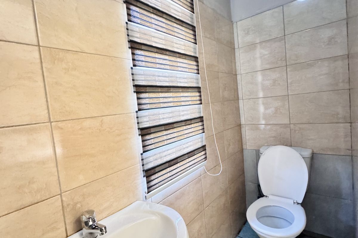 A compact bathroom featuring a pedestal basin, toilet, and tiled walls. The space shows signs of wear and requires maintenance.