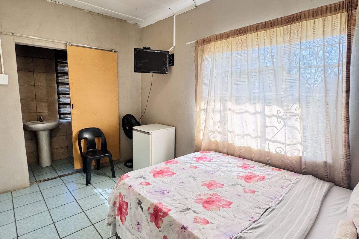 A compact bedroom featuring tiled flooring, a window with security bars, and an attached en-suite bathroom with a pedestal basin.