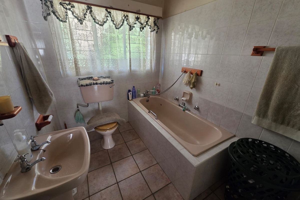 A dated bathroom featuring a peach-colored bathtub, matching pedestal sink, and toilet, with tiled walls and flooring.