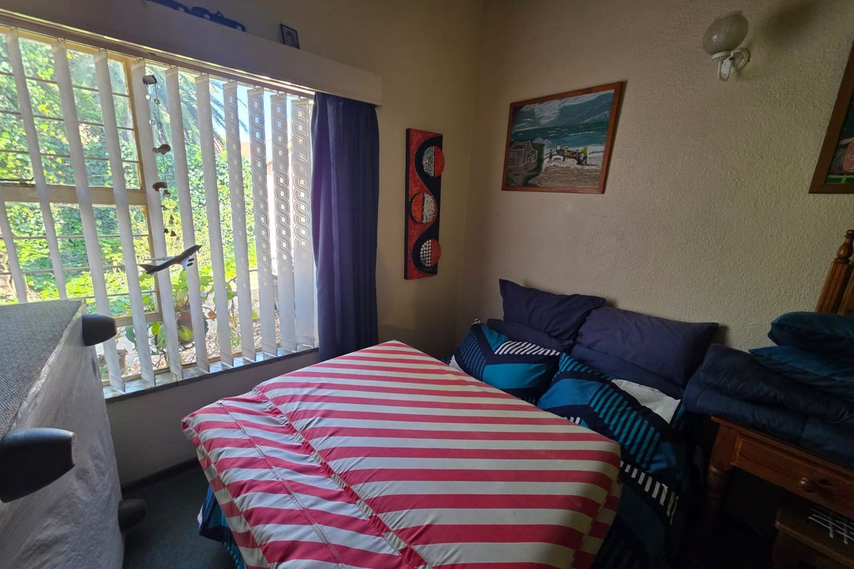 A bedroom featuring a large window with vertical blinds, textured walls, and a wall-mounted light fixture.