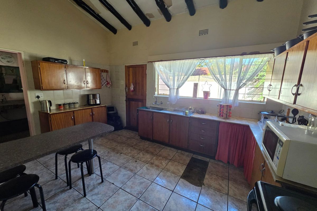 A dated kitchen featuring wooden cabinetry, tiled flooring, and exposed ceiling beams, offering significant potential for renovation and modernization.