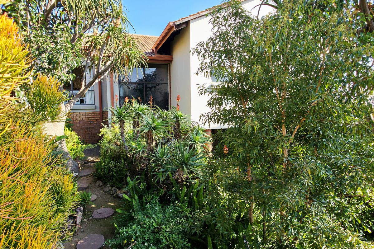 A view of the rear building elevation featuring brick and plaster finishes, a tiled roof, and a stone pathway surrounded by established garden foliage.