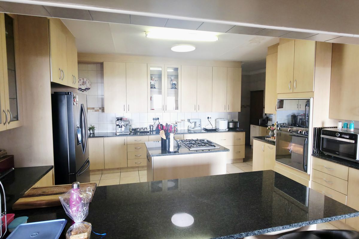 Spacious kitchen featuring light wood cabinetry, granite countertops, a central island with a gas hob, and integrated oven, offering ample storage and workspace.