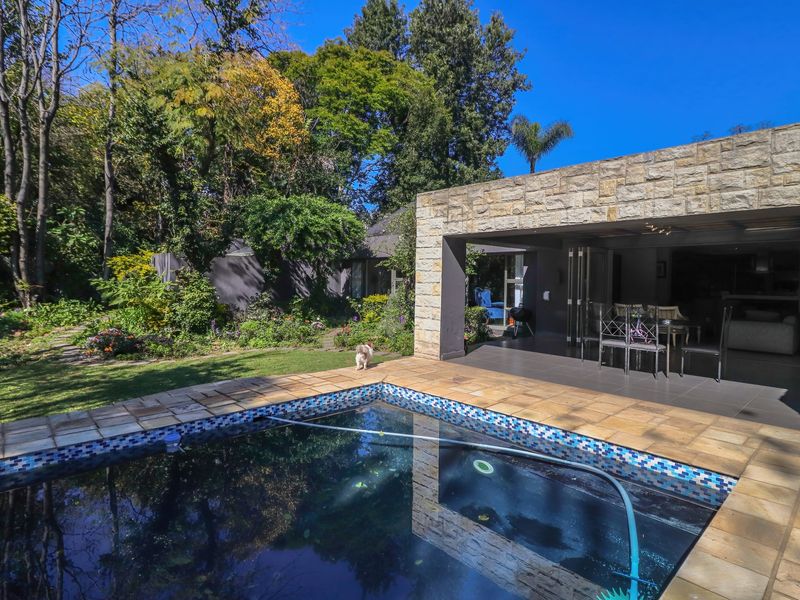 A well-maintained outdoor area featuring a swimming pool with stone paving, adjacent to a covered patio and lush garden surroundings.
