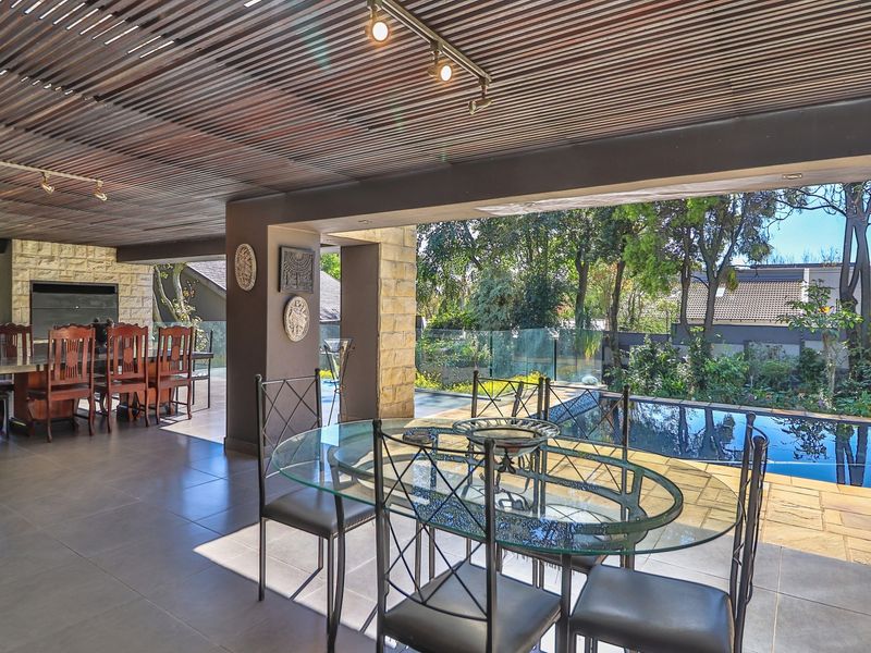 Spacious covered patio featuring a built-in braai, timber slat ceiling, and tiled flooring, overlooking a private swimming pool and landscaped garden.