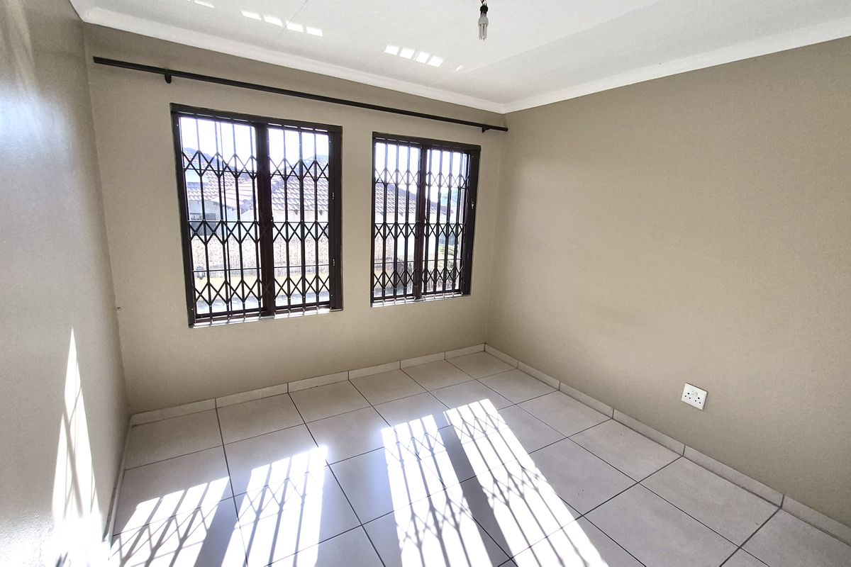 A bright, empty bedroom featuring neutral tiled flooring, painted walls, and security bars on the windows.