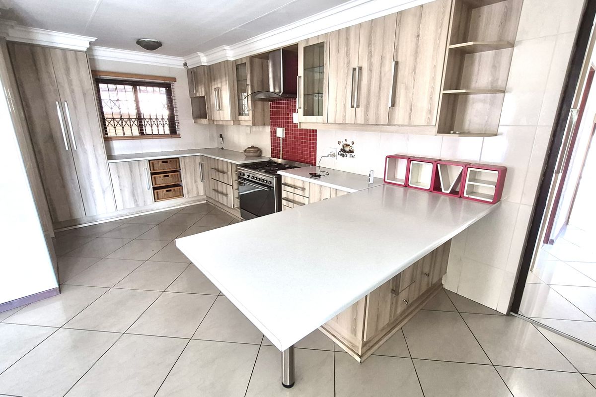 A functional kitchen featuring light wood-grain cabinetry, a red tiled backsplash, a built-in oven with extractor fan, and a white breakfast bar island.