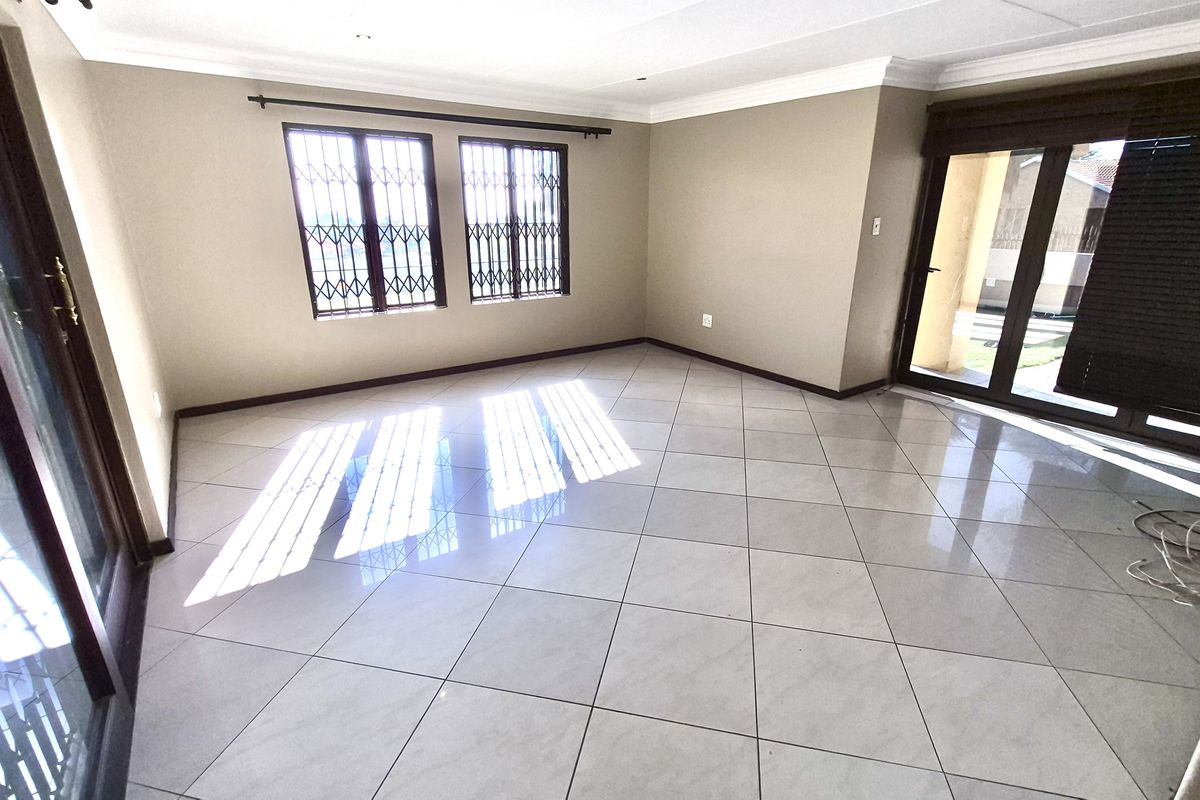 A bright, spacious living room featuring neutral wall tones, large ceramic floor tiles, and multiple glass sliding doors providing access to the exterior.