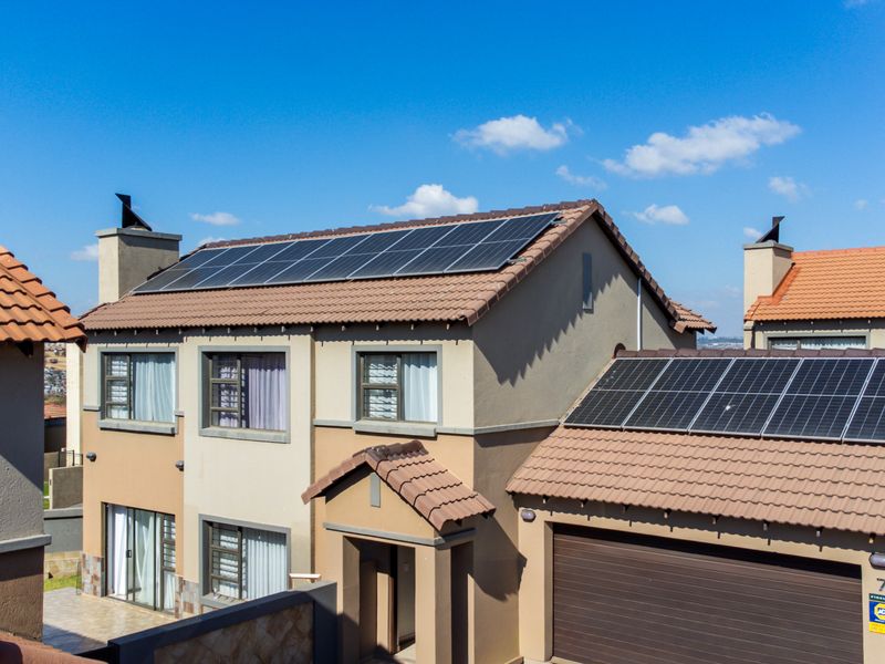 Front elevation of a double-storey townhouse featuring a tiled roof, integrated solar panel system, and a secure garage.