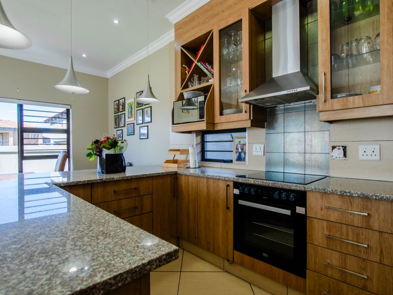 Modern kitchen featuring warm wooden cabinetry, granite countertops, built-in oven, electric hob, and stainless steel extractor fan with ample storage and display space.