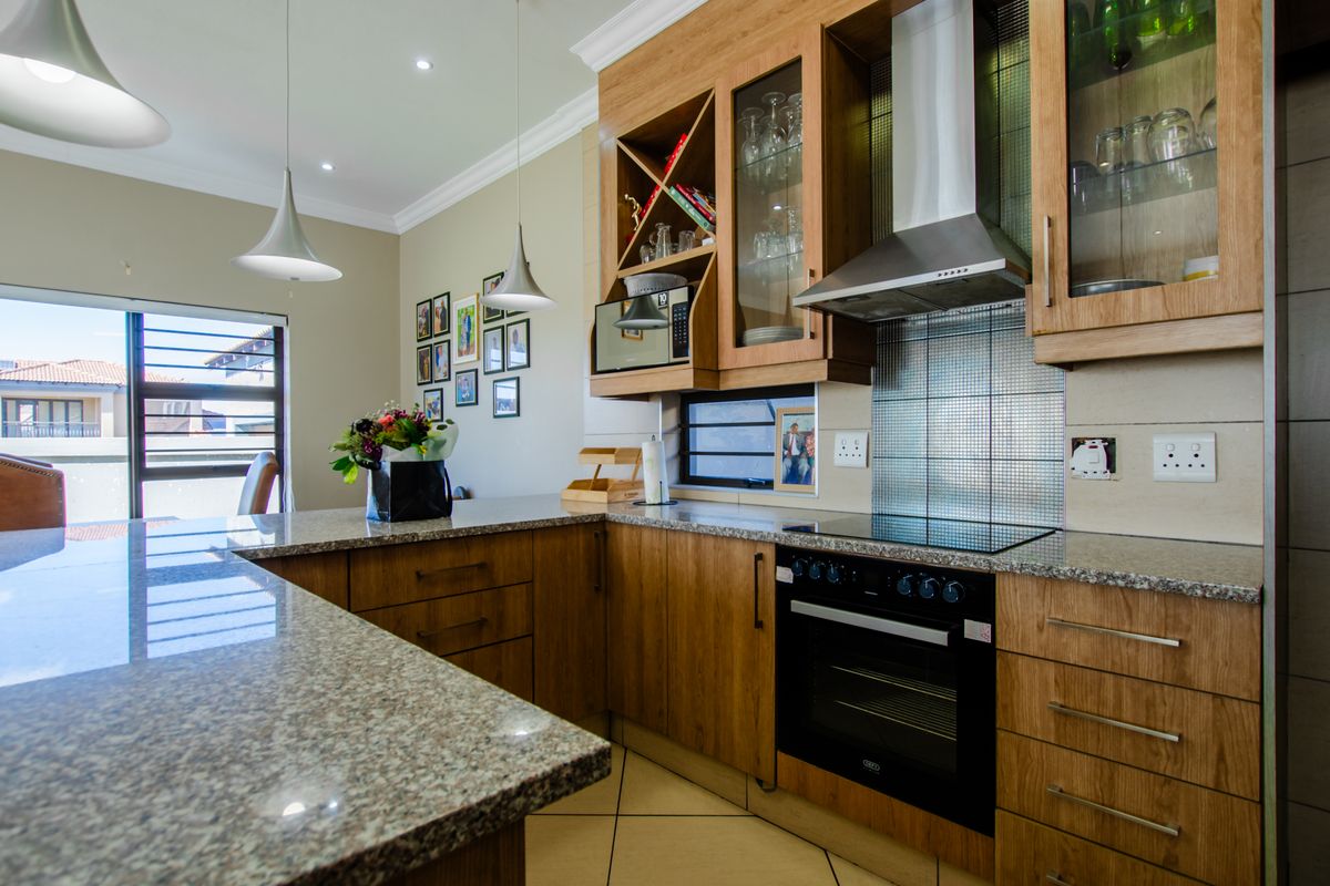 Modern kitchen featuring warm wooden cabinetry, granite countertops, built-in oven, electric hob, and stainless steel extractor fan with ample storage and display space.