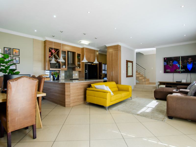 Spacious open-plan living area featuring a modern kitchen with wood-finish cabinetry, stone countertops, and tiled flooring, seamlessly flowing into the lounge and dining space.