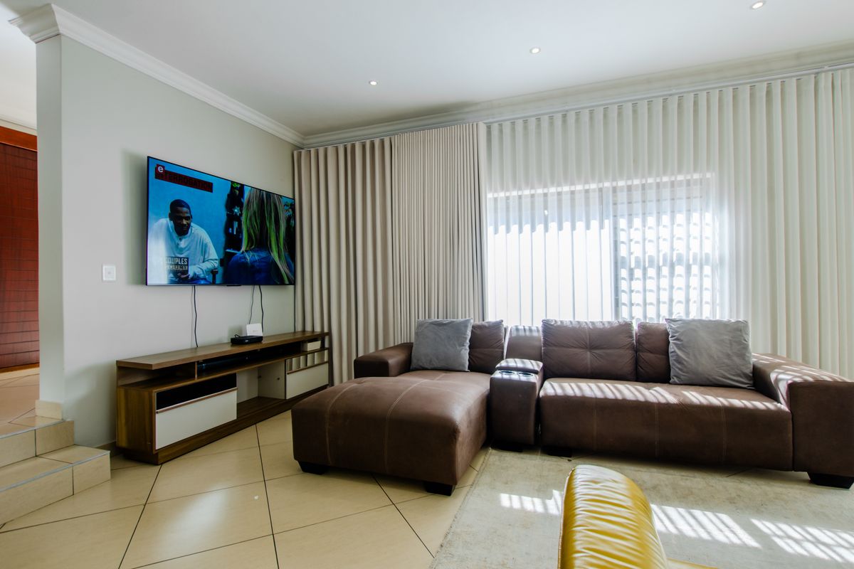 A well-maintained living room featuring tiled flooring, recessed downlighting, and floor-to-ceiling curtain tracks, creating a bright and functional living space.