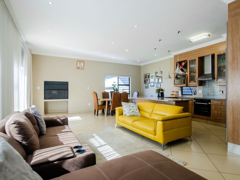 Spacious open-plan living and dining area featuring a modern kitchen with built-in appliances, stone countertops, and tiled flooring throughout.