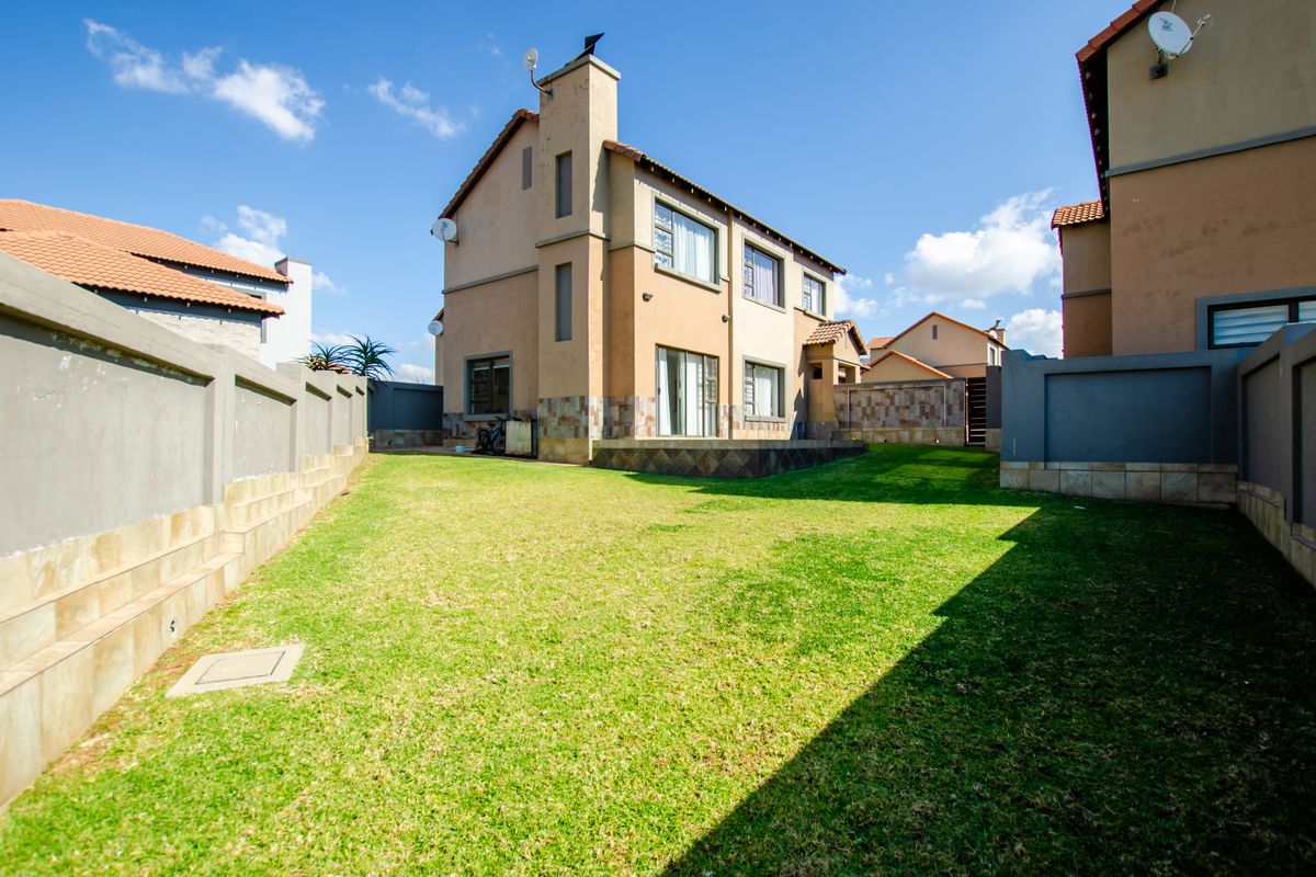 A spacious rear garden featuring a well-maintained lawn, perimeter boundary walls, and a multi-story townhouse exterior with stone cladding and sliding door access.