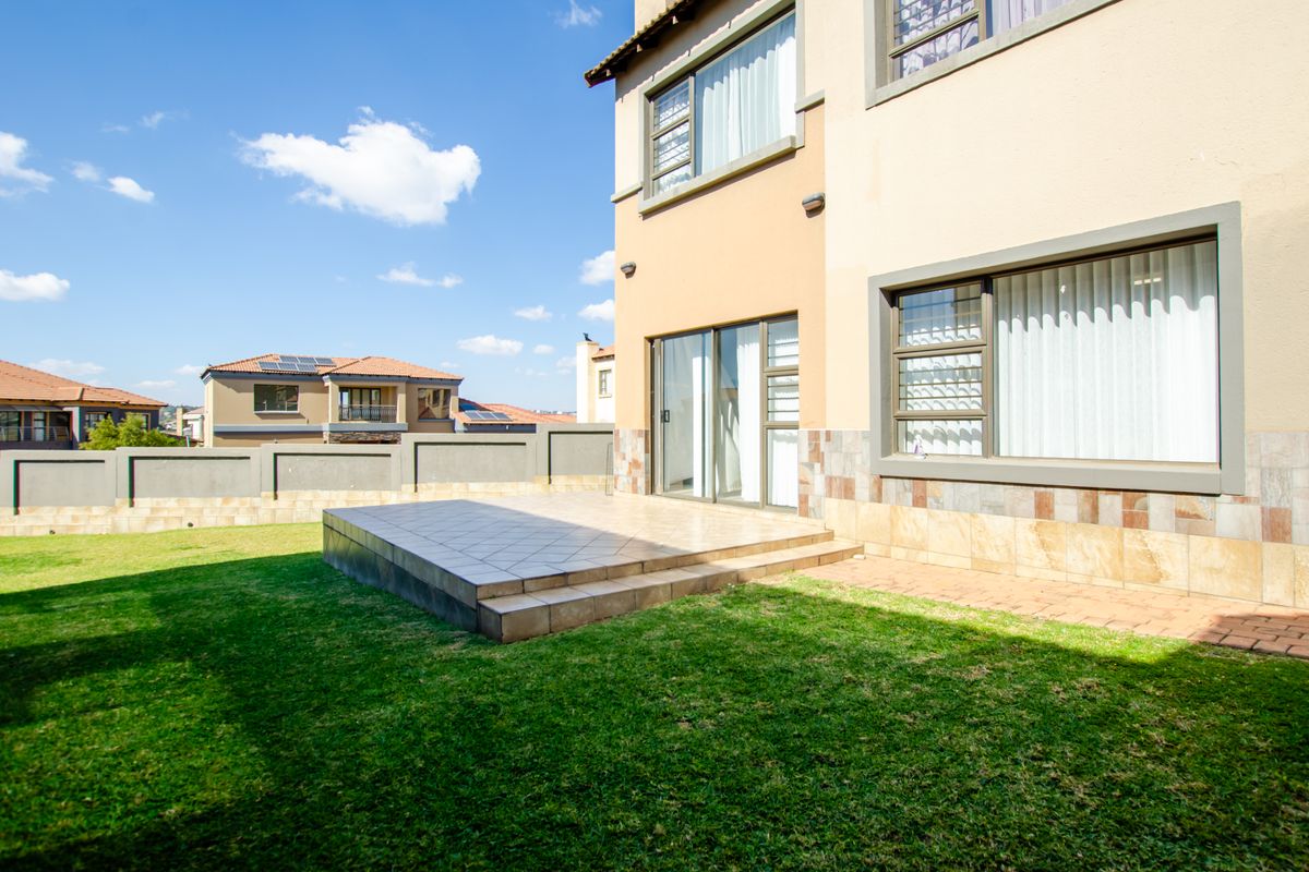 Rear view of the townhouse featuring a raised tiled patio, landscaped garden, perimeter wall, and sliding door access to the interior living space.