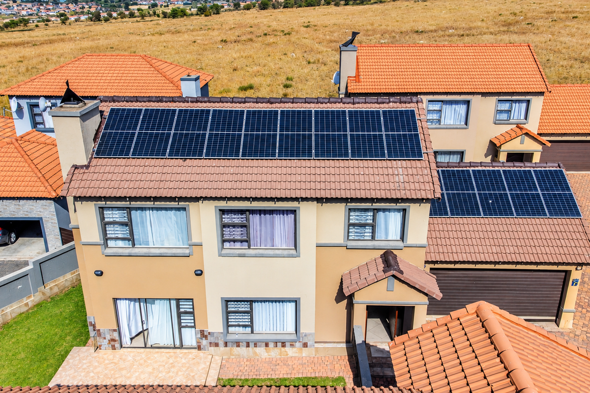 Aerial view of a townhouse featuring a tiled roof with extensive solar panel installation, paved driveway, and attached garage.