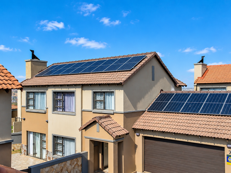 A well-maintained townhouse exterior featuring a tiled roof, integrated solar panel arrays, and a secure garage entrance.