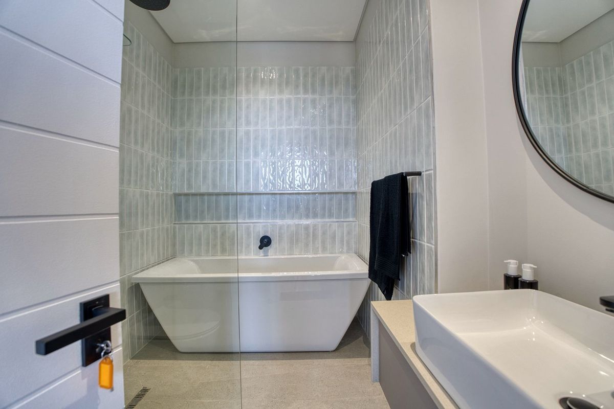 Modern bathroom featuring a freestanding bathtub, glass shower screen, wall-mounted matte black fixtures, and contemporary tiled wall finishes.