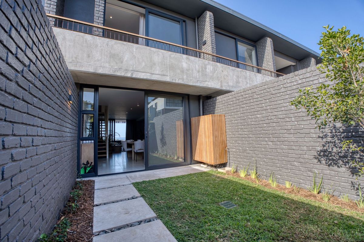 A modern rear exterior view featuring a private garden, paved walkway, and sliding glass doors leading into the open-plan living area.