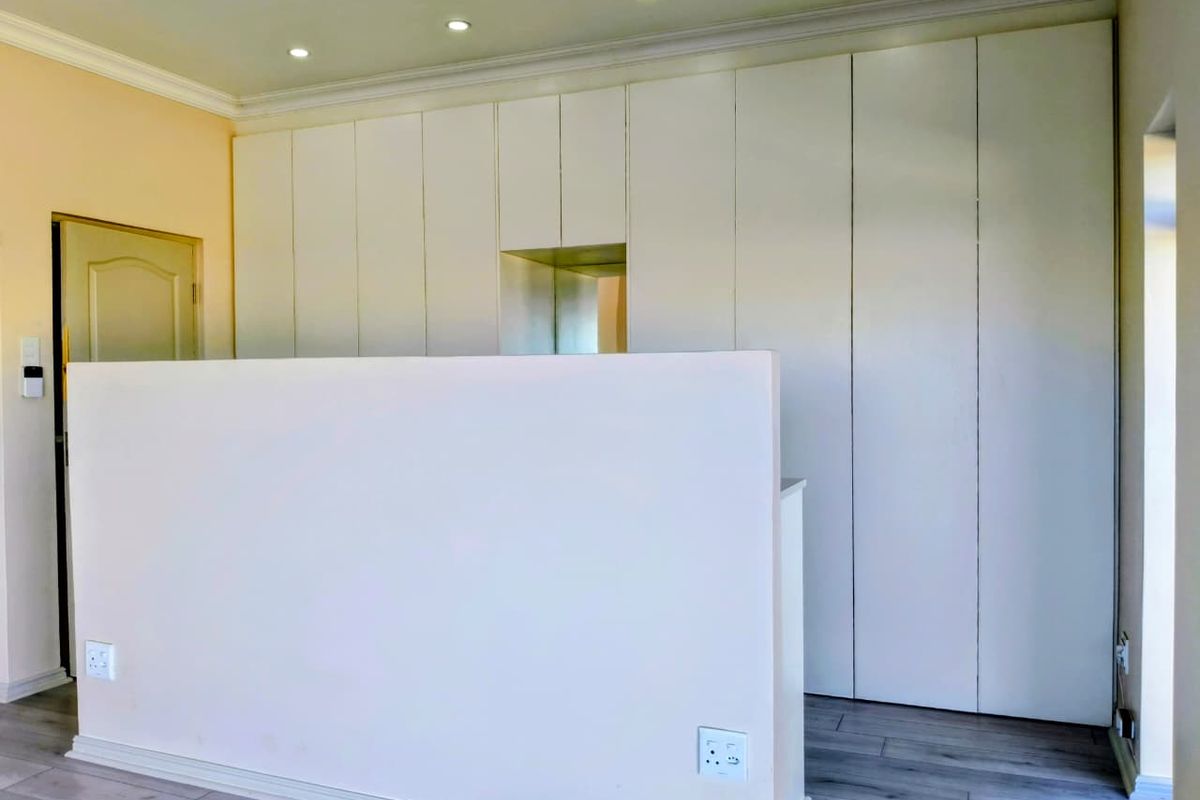 A bright bedroom featuring extensive floor-to-ceiling built-in cabinetry, recessed ceiling lighting, and modern wood-look flooring.
