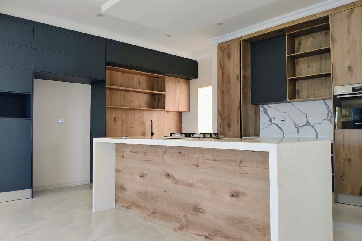 Modern kitchen featuring a large central island with stone countertop, integrated oven, dark cabinetry, and wood-grain accents.