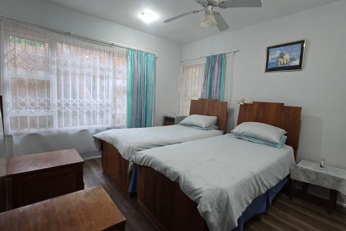 A bedroom featuring wood-look flooring, a ceiling fan, and large windows with security bars.