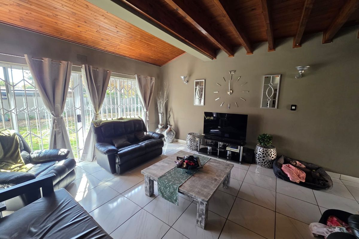 Spacious living room featuring high vaulted timber ceilings with exposed beams, large sliding glass doors with security gates, and polished floor tiles.