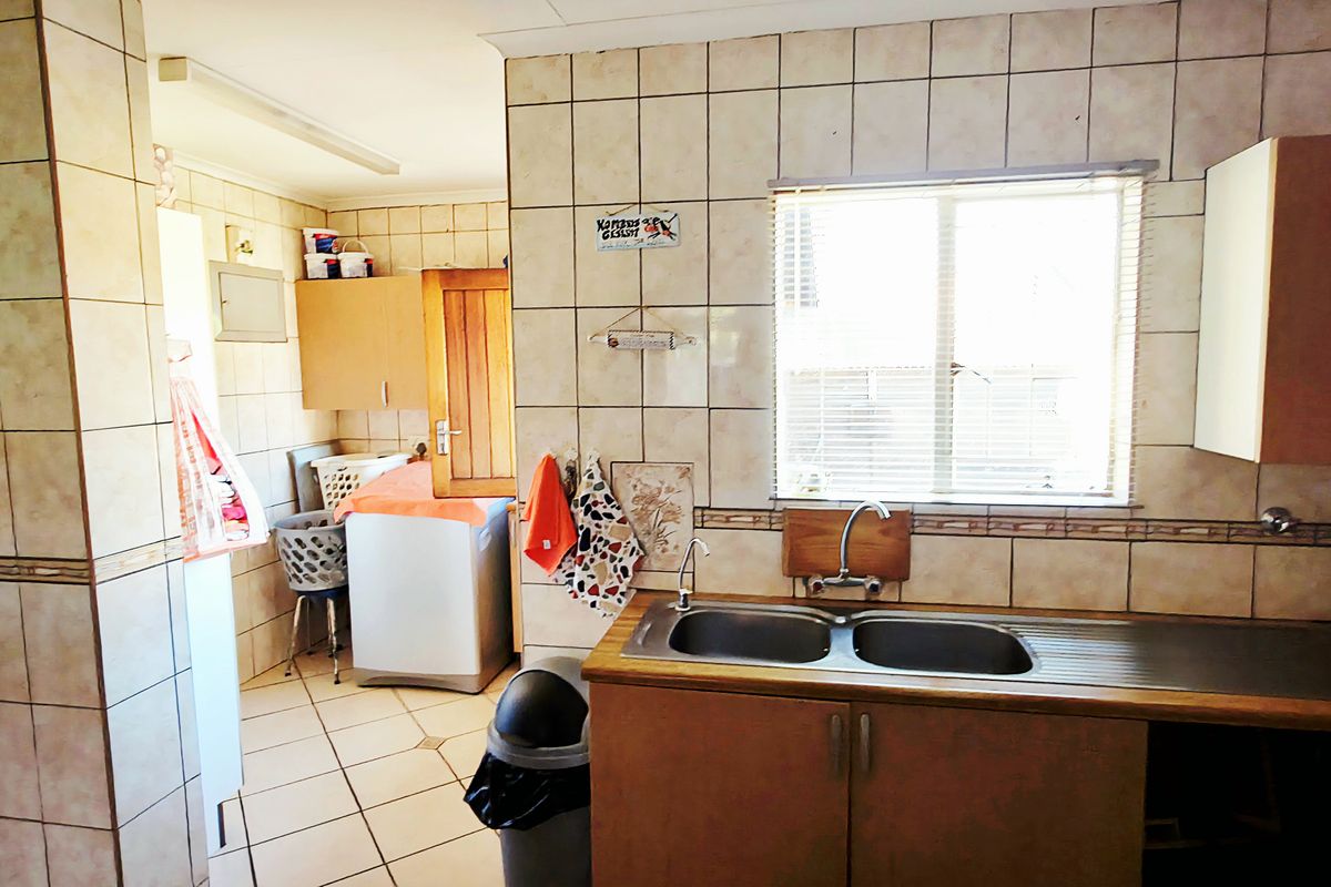 A functional kitchen featuring tiled walls, double basin sink, and built-in cabinetry, with an adjacent utility area for laundry appliances.