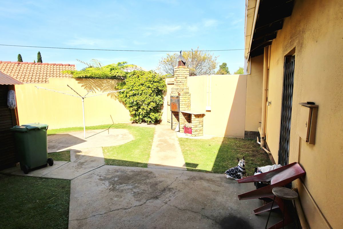 A private rear garden featuring a built-in brick braai, concrete pathways, and a small lawn area enclosed by perimeter walls.