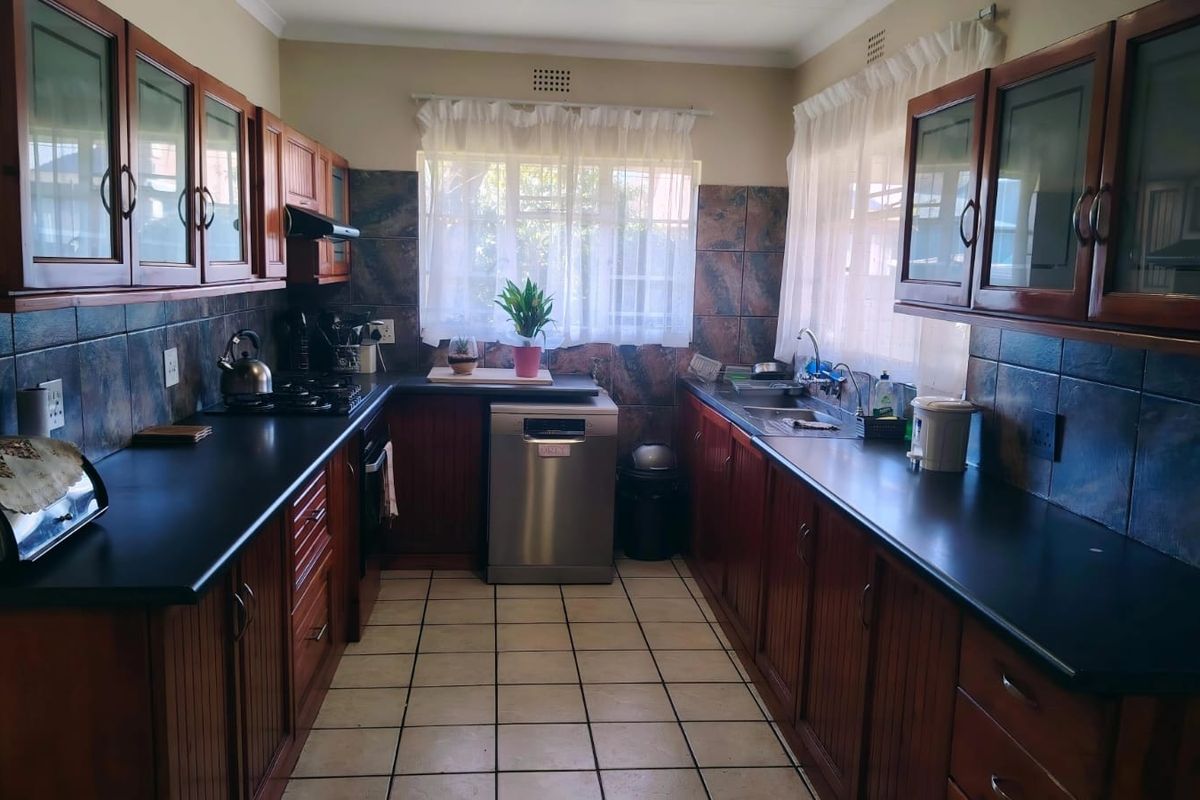 A functional galley-style kitchen featuring dark wood cabinetry, black countertops, tiled splashbacks, and ceramic floor tiles with dual windows for natural light.