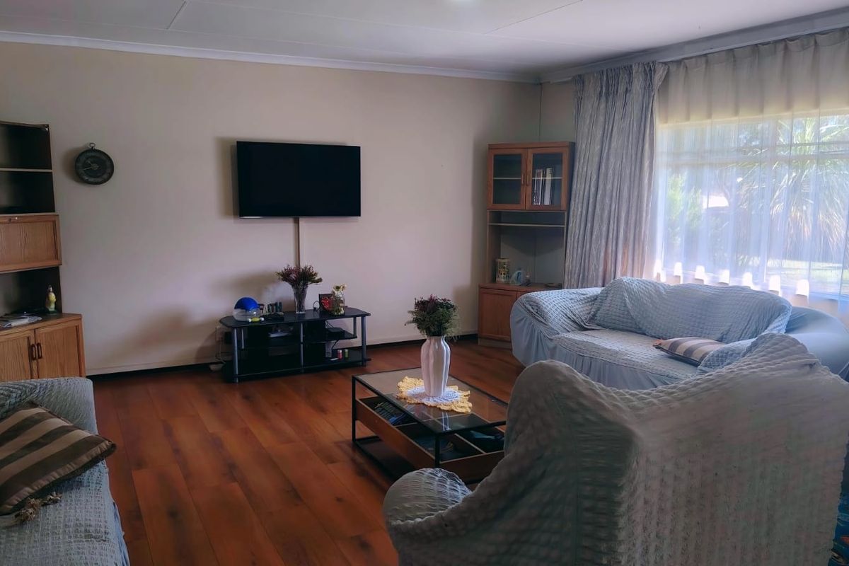 A comfortable living room featuring warm-toned laminate flooring, large windows with curtains, and a neutral wall finish.