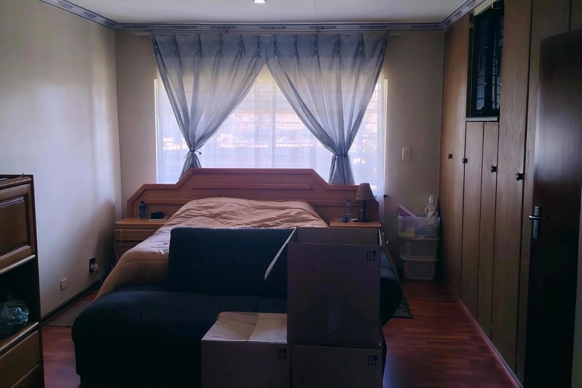 A bedroom featuring built-in wooden wardrobes, laminate flooring, and a large window with curtains.