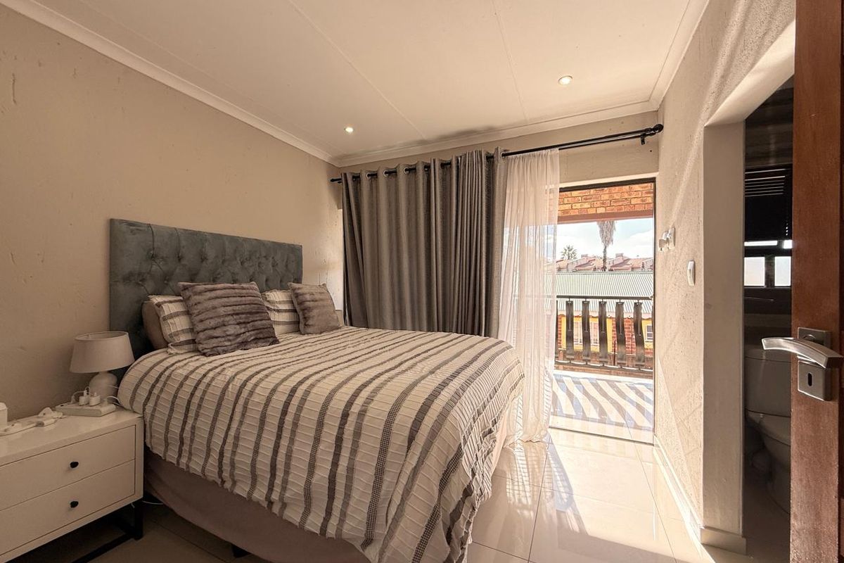 A well-lit bedroom featuring tiled flooring, recessed lighting, and direct access to a private balcony through a sliding door.